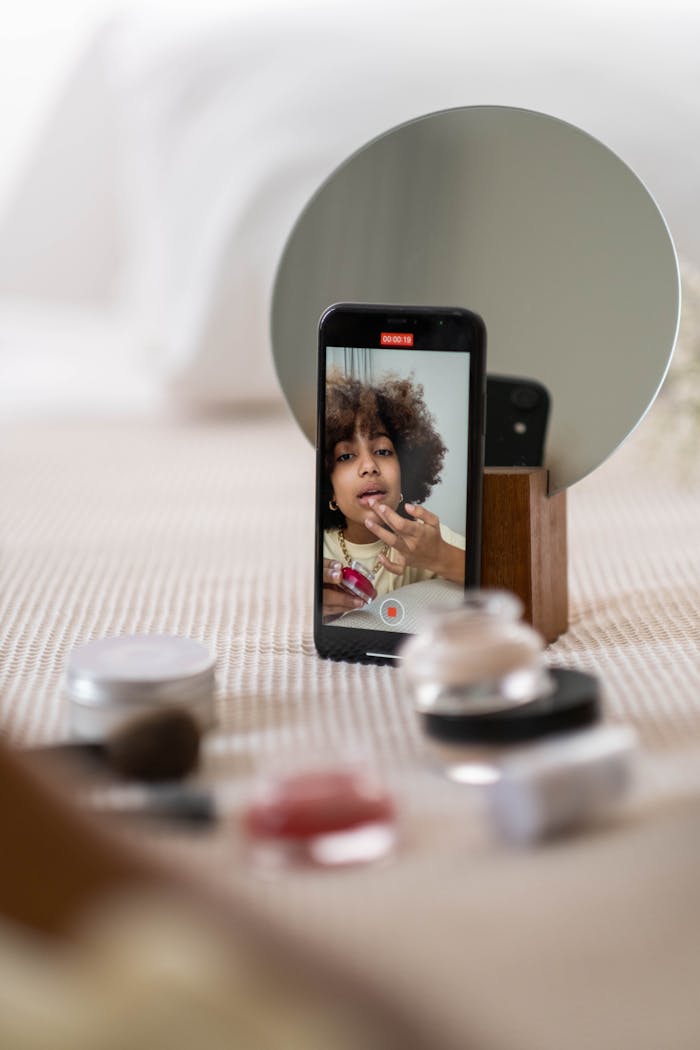 A beauty influencer vlogs a makeup tutorial using a smartphone indoors.